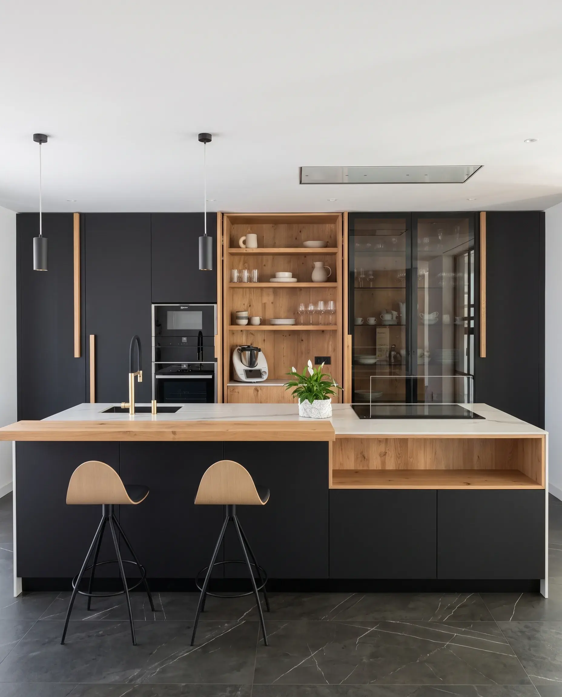 Cocina montada por Komad: columnas negras con vitrina, estantería de roble e isla de mármol con barra de roble